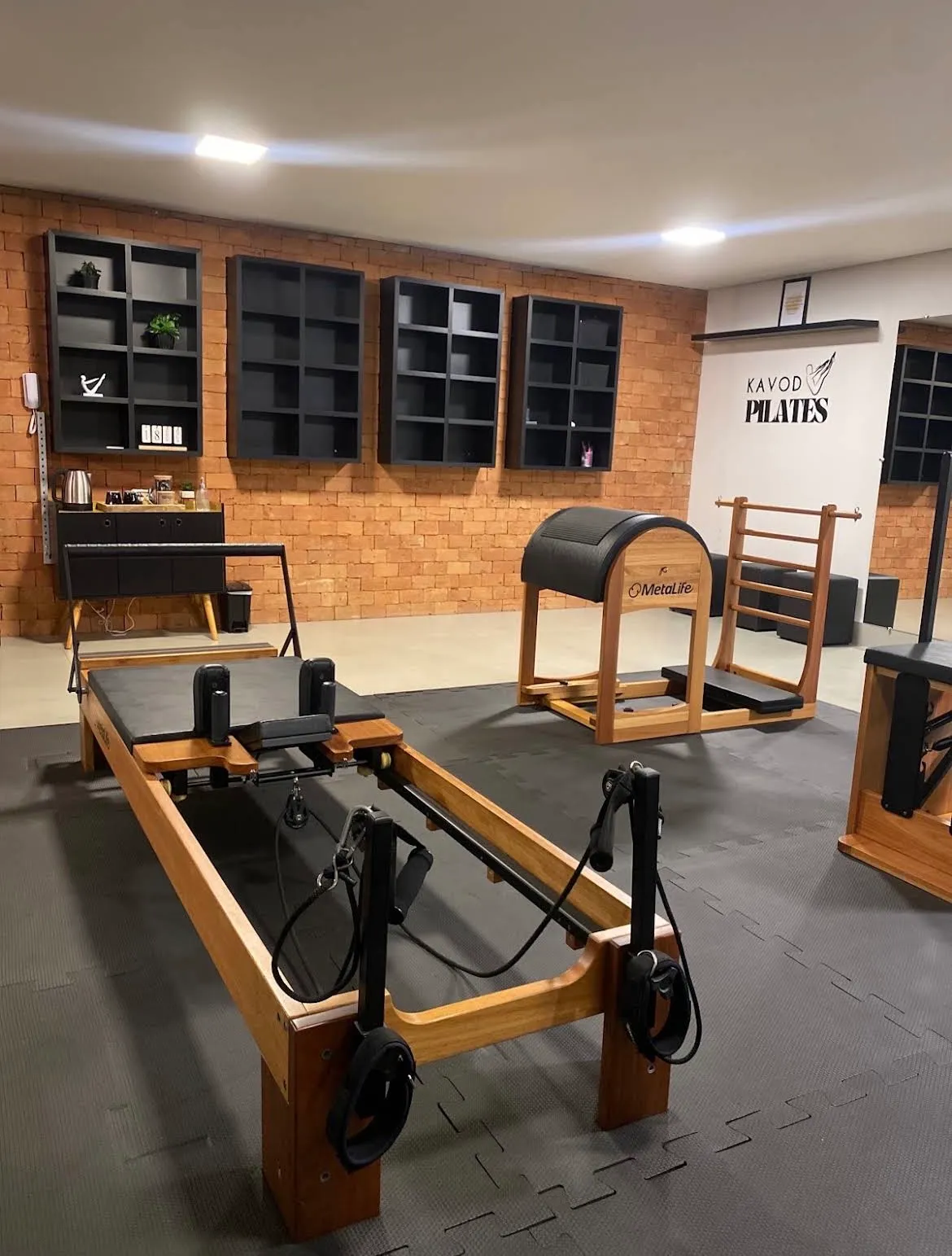 Reformer e Ladder Barrel no estúdio, com parede de tijolos e o logo Kavod Pilates ao fundo